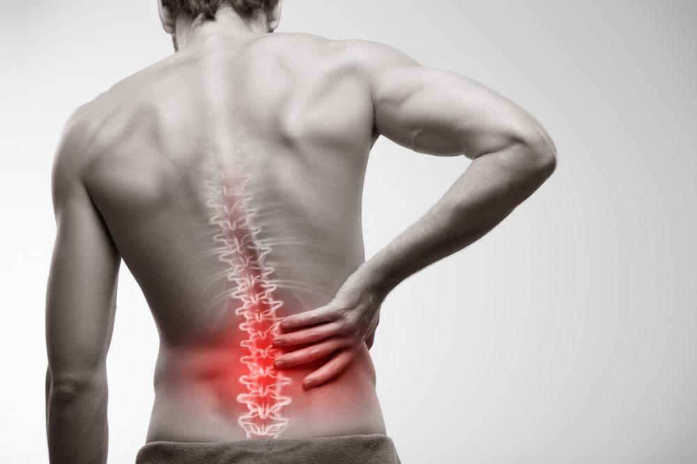 A man standing with a pained expression, holding his lower back, indicating discomfort from back pain